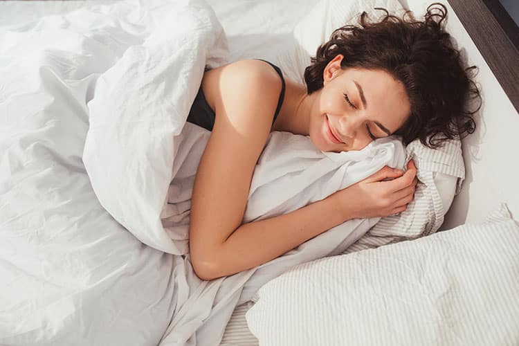 Eine junge Frau schläft glücklich in einem Bett.