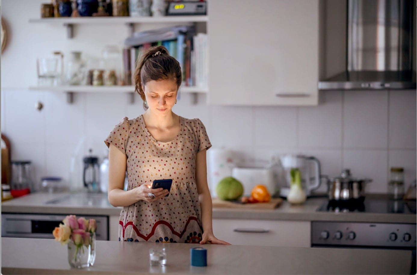 Eine Frau steht in der Küche und schaut auf ihr Handy