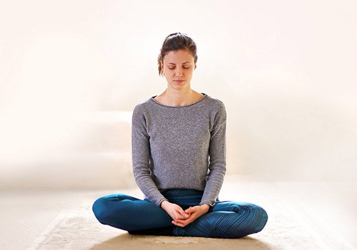 Eine junge Frau sitzt mit geschlossenen Augen im Schneidersitz und meditiert.