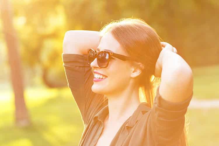 Eine glückliche Frau mit Sonnenbrille schaut in die Ferne und verschränkt die Arme hinterm Kopf.
