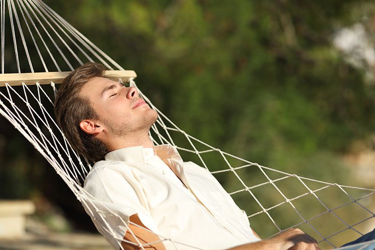 Ein junger Mann genießt seinen Mittagsschlaf auf einer Hängematte in der Sonne.