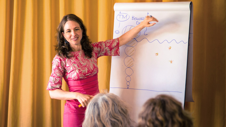 Eine TM-Lehrerin erklärt Zuhörern etwas auf einem Flipchart