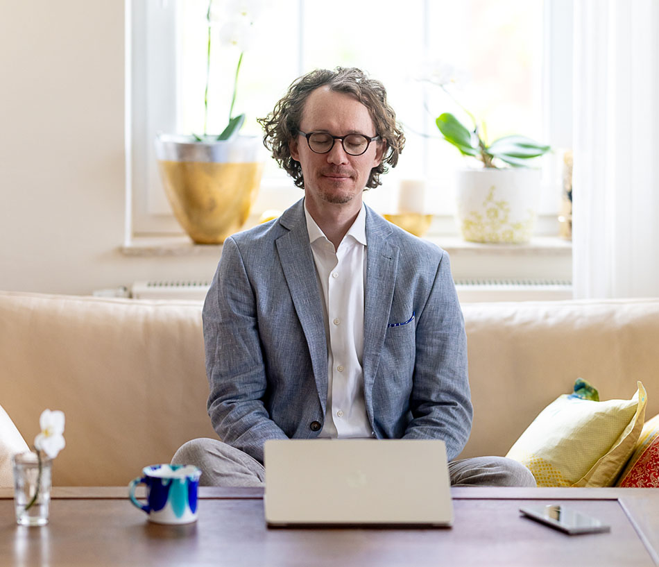 Ein junger Mann sitzt mit geschlossenen Augen vor einem Laptop und meditiert